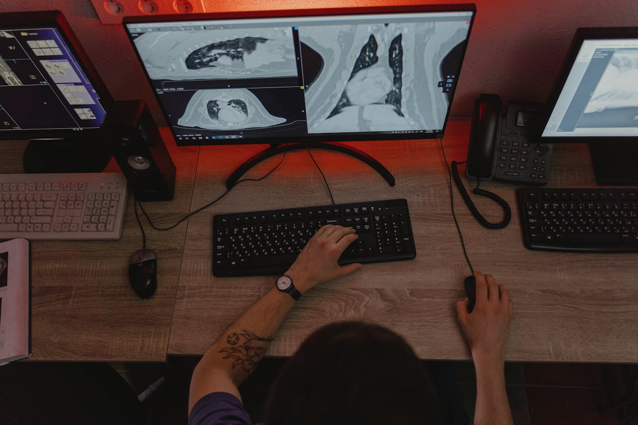 A radiologist reviews x-ray scans on multiple monitors at a desk, focusing on medical diagnostics.